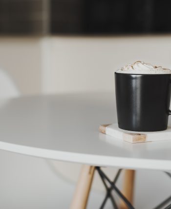 Coffee with whipped cream and cinnamon powder served in a black mug on a marble coaster